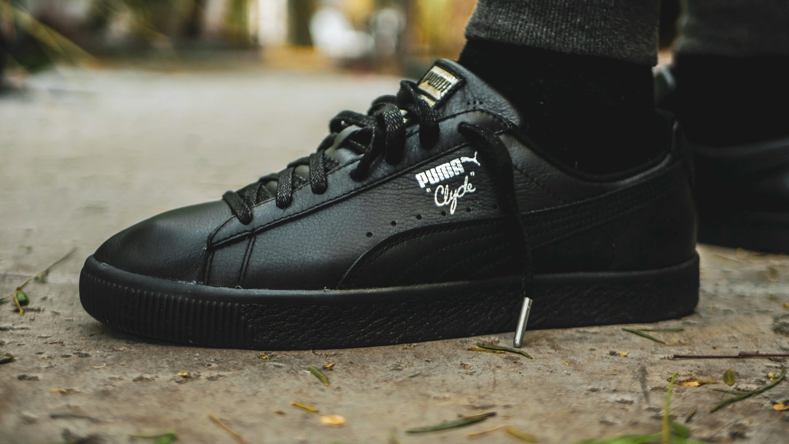 Close-up of black Puma Clyde sneaker on a textured outdoor surface, showcasing fashion and style.